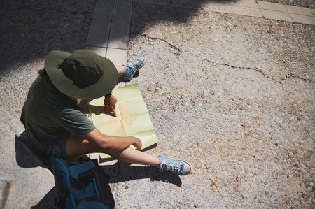 An adventurer consults a map in a sunny historic town, showcasing exploration, planning, and outdoor travel amidst medieval surroundings with a backdrop of natural beauty.の写真素材