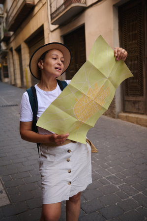 A woman tourist holding a map navigates through scenic urban streets, wearing casual attire. The image captures exploration and travel vibes, showcasing the charm of city architecture and culture.の写真素材