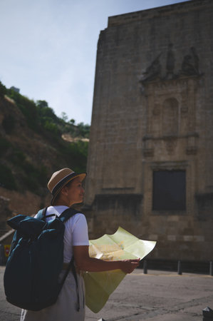 A female tourist examines a map while exploring an ancient town's landmarks under sunny skies,...