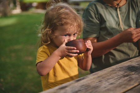 A young child enjoys a drink outdoors while spending time with family in a peaceful natural setting. A delightful moment of nature, lifestyle, and family connection in a rustic environment.の写真素材