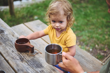 A charming scene of a young child sitting outdoors with drinks, enjoying a moment in nature. Family and outdoor living inspire warm feelings and cherished memories.の写真素材