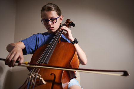 A young musician plays a cello with focus and dedication, highlighting creativity and the passion for music in an isolated indoor setting.の写真素材