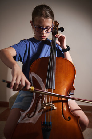 A young musician, wearing glasses, plays the cello with concentration in a bright room, highlighting the musician's true passion for classical instruments.の写真素材