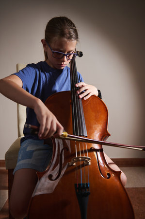 A young girl wearing glasses practices the cello in a calm indoor setting, illustrating musical passion and dedication.の写真素材