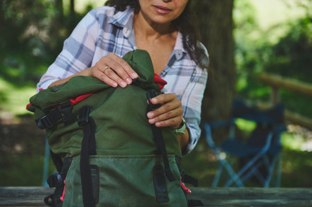 A woman organizing her green hiking backpack outdoors, depicting adventure and preparation in...