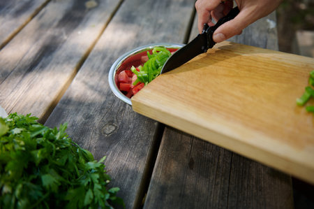 A close-up view of fresh vegetables being cut and prepared for a meal outdoors on a wooden surface.
