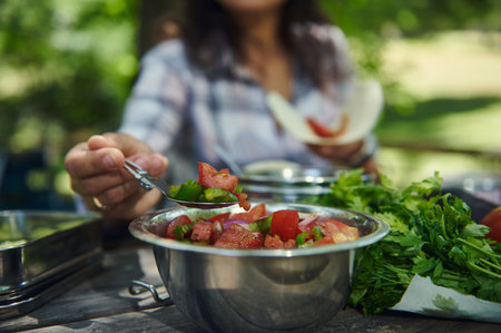 A vibrant, fresh vegetable salad is served outdoors in a serene park setting on a sunny day. Fresh chopped tomatoes and greens are complemented by natural light, evoking feelings of joy and health.の写真素材