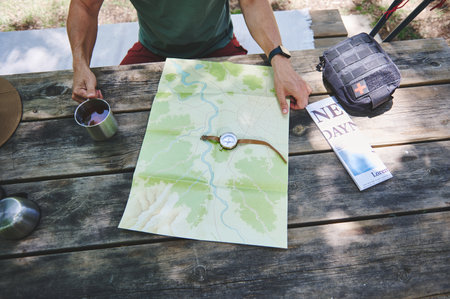 A hands-on scene featuring an individual consulting a map and compass on a wooden table outdoors. Outdoor gears are visible, expressing adventure, navigation, and outdoor activities.の写真素材