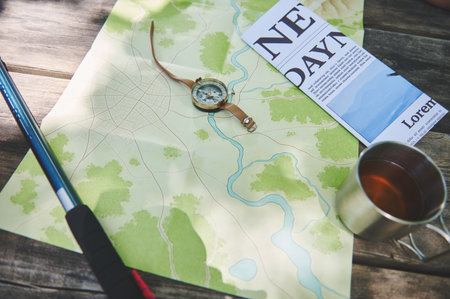 An outdoor setup featuring camping essentials like a map, compass, and hiking pole placed on a wooden table, evoking adventure and exploration.の写真素材