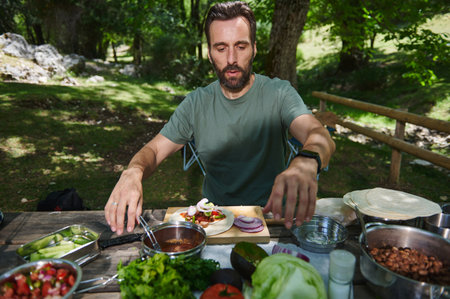 A man makes a fresh meal outdoors surrounded by lush trees and sunlight, enjoying a nature getaway, showcasing healthy, balanced eating in a serene environment.の写真素材