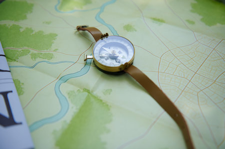 A compass with a leather strap placed on a detailed map showing a river and surrounding greenery,...