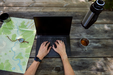 Image depicting a workspace outdoors with a laptop, map, compass, and coffee. Represents remote work, adventure planning, and efficient multitasking in a serene natural setting.の写真素材