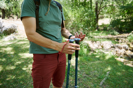 An individual is seen preparing trekking poles in a lush woodland setting, symbolizing outdoor exploration and active lifestyles. Ideal imagery for adventure, travel, and nature themes.の写真素材