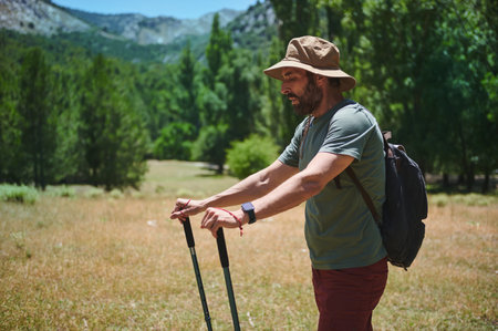 A man in his 40s outdoors, exploring stunning mountain scenery with hiking poles, a wide-brimmed hat, and a backpack, emphasizing travel, camping, and adventure. Active lifestyle inspiration.の写真素材