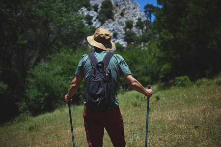Explorer wearing hat and backpack hikes with trekking poles under blue skies, embracing nature's beauty and adventure. Perfect representation of outdoor pursuits and adventurous lifestyle.の写真素材