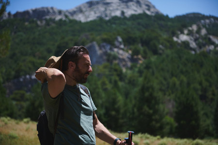 A man hiking through a picturesque mountain area, equipped with outdoor accessories and enjoying a sunny summer day, embodying adventure and nature's beauty.の写真素材