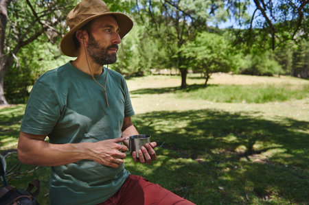 A bearded traveler savors his moment during a sunny summer adventure in a serene mountain location. The man embraces the joy of nature and outdoor exploration.の写真素材