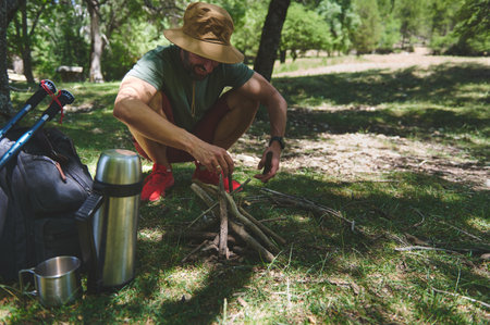 A man in nature preparing a campfire for an outdoor activity surrounded by equipment. The scene reflects adventure, wilderness exploration, and an active outdoor lifestyle.の写真素材