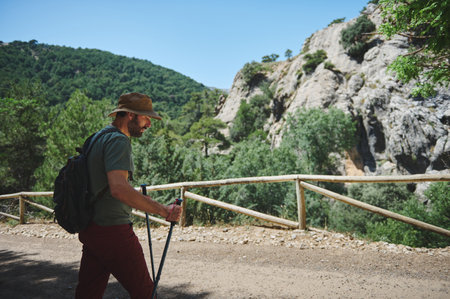A traveler with hiking gear walking along a lush green mountain trail amidst clear blue skies. Captivates the essence of exploration, nature, and serenity on a summer day.の写真素材