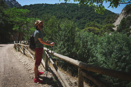 A man walking on a trail surrounded by lush green mountains, embodying adventure and an active lifestyle. His backpack and walking sticks illustrate passion for outdoor exploration and nature.の写真素材