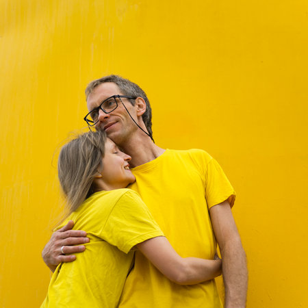 A joyful moment shared by a couple dressed in matching yellow shirts, standing against a bright...