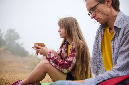 Two hikers rest in a serene mountain setting, with soft natural lighting and misty background....