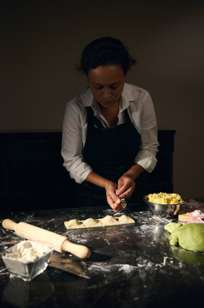 A woman chef crafts ravioli using tricolor dough in a dimly lit kitchen. The process emphasizes...