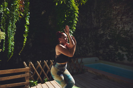 A woman practices yoga outdoors in a serene garden with lush greenery, embracing wellness amid...