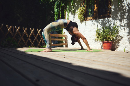 A woman practices yoga on a wooden deck, performing a backbend posture in a vibrant, outdoor setting...