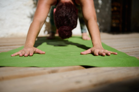 Woman practicing a yoga pose on a balcony, focusing on her hands on a green mat, capturing tranquility and balance in a sunny environment.の写真素材