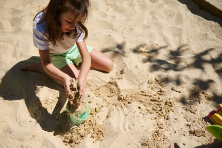 A cheerful girl playing with sand on a sunny day, engaging in creative outdoor activities. The scene captures childhood joy, imagination, and carefree fun under natural light.の写真素材