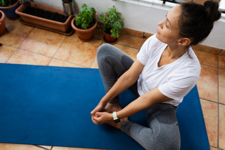 A serene moment captured as a woman focuses on her yoga practice, sitting on a blue mat surrounded...