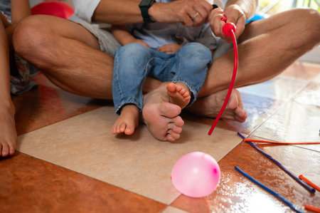 A family interacts on a tiled floor blowing and playing with balloons and colorful sticks, creating joyful memories. The scene highlights togetherness and fun activities within a cozy home environment.の写真素材