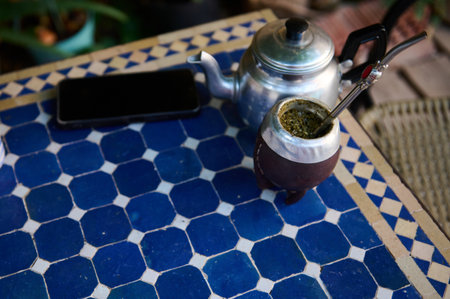 Yerba Mate beverage in a traditional gourd with a straw, accompanied by a kettle, sitting on a decorative blue tiled table, evoking cultural warmth and casual ambiance.の写真素材