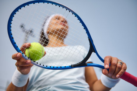 A dynamic shot featuring a female tennis player holding a racket and tennis ball, depicting anticipation and readiness, emphasizing fitness and determination on a clear day.の写真素材