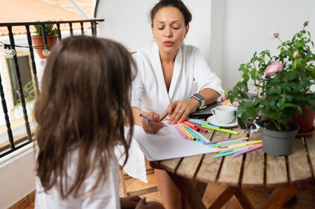 A charming scene of a mother and daughter drawing together on a cozy balcony, emphasizing creativity and bonding.の写真素材