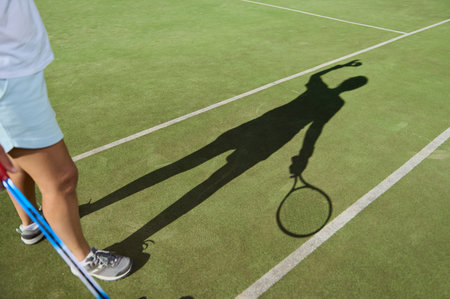 The dynamic shadow of a tennis player performing a serve on a vibrant green court captures the energy of sports and outdoor activity.の写真素材