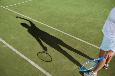 A tennis player's shadow is cast on a green court surface, depicting action during a match under bright sunlight. Vibrant and dynamic atmosphere is captured, symbolizing the sport's energy.の写真素材