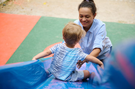 A joyful interaction between a mother and her toddler while playing on a slide in a vibrant...
