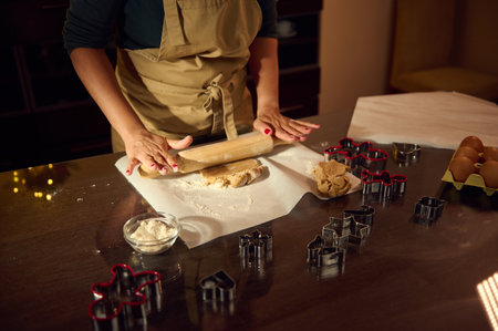 A woman preparing festive gingerbread cookies on a countertop surrounded by utensils, cookie...