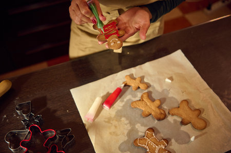 A woman decorates gingerbread cookies with icing in a cozy kitchen during the holidays. Cookie...