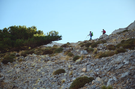 Two hikers traverse a rugged, rocky terrain, enjoying outdoor trekking amidst nature's serene beauty. The scene highlights adventure and exploration under a bright and clear sky.の写真素材