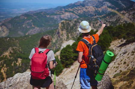 Two hikers explore a breathtaking mountainous landscape, equipped with backpacks and trekking gear....