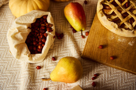 Autumn harvest still life with cranberries in a bag, pears, an apple, and a latticed pie on a wooden board. Cozy table setting for Thanksgiving and fall cooking scenes.の写真素材