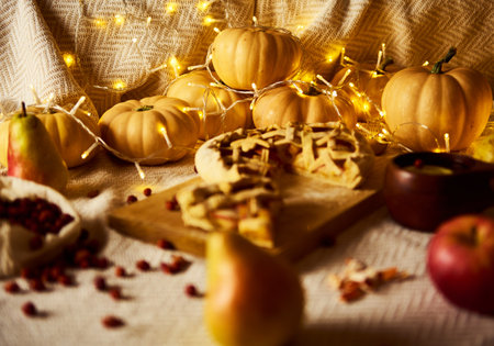 A warm autumn still life featuring pumpkins, apples, a lattice pie, and twinkling lights on a...