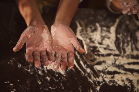 Warm scene of floury hands on a dark wooden table, family baking together with dough and flour, conveying home, warmth, and festive cooking.の写真素材