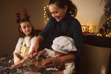 Warm, festive moment of a mother guiding two children in baking gingerbread at home, with Christmas...