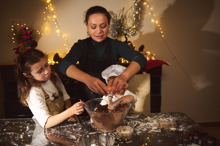 A mother and two children bake gingerbread in a warmly lit kitchen. Holiday lights and festive decor create a cozy Christmas scene as they mix dough and decorate treats, celebrating family togetherness during the holiday season.の写真素材