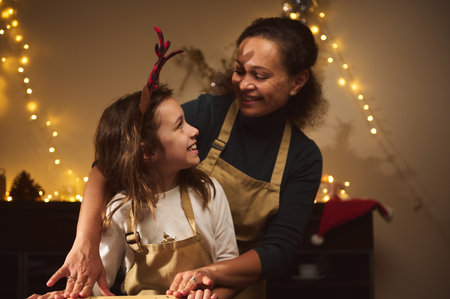 A smiling mother with a child, both wearing beige aprons, share a playful Christmas moment amid warm...