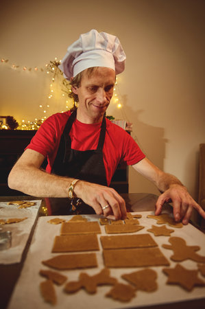A baker in a red shirt and white chef hat shapes gingerbread cookies on a tray in a cozy home...